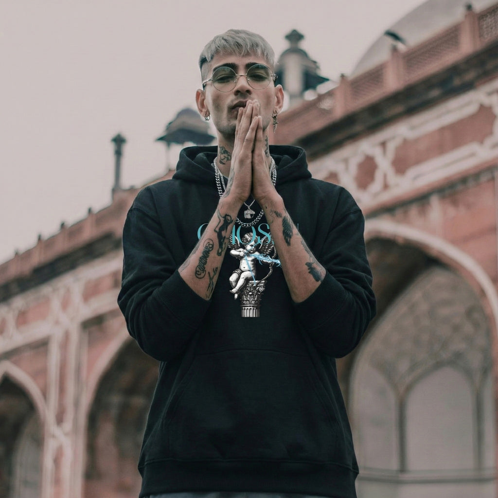 Man in black hoodie with tattoos and sunglasses in front of architectural background
