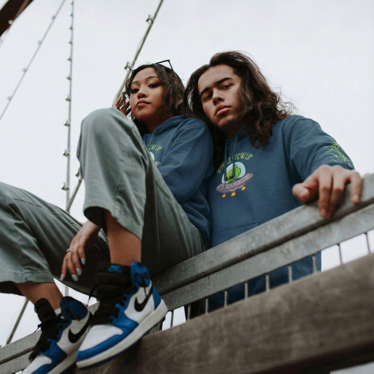 Two people sitting on a bridge, wearing matching blue sweatshirts.